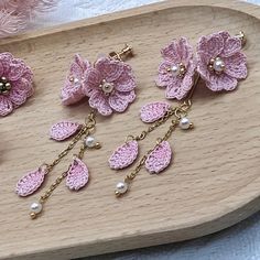 pink crocheted flowers and pearls are on a wooden tray next to some beads