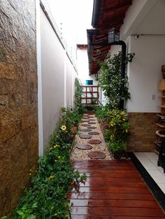 a long narrow walkway between two buildings with plants growing on the sides and an open door leading to another building