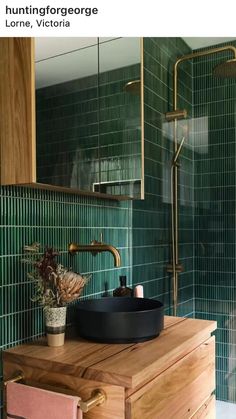 a bathroom with green tiled walls and wooden cabinet, black bowl sink and gold faucet