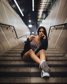 a woman is sitting on the stairs talking on her cell phone and looking at the camera