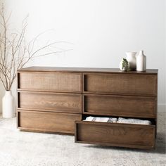 a large wooden dresser with drawers and two vases on top of it in front of a white wall