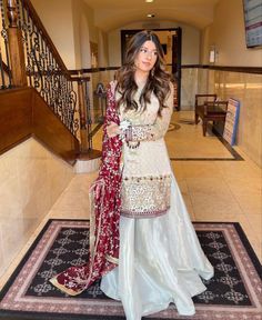 a woman standing on top of a rug wearing a white and red dress with gold accents