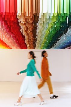 two women walking in front of a multicolored art work on the wall behind them