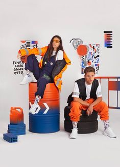 a woman sitting on top of a giant orange barrel next to a boy in white shirt