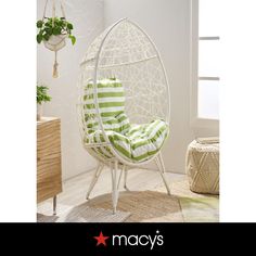 a white chair with green and white striped pillows on it's back, next to a potted plant