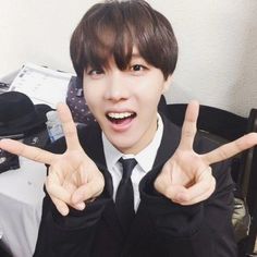 a young man in a suit and tie making the peace sign with his hands while sitting at a desk