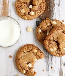 three cookies with white chocolate chips next to a glass of milk