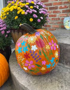 an orange painted pumpkin sitting on top of a cement slab next to flowers and potted plants