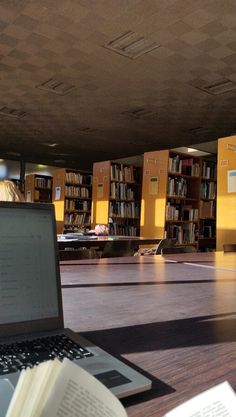 an open laptop computer sitting on top of a wooden table next to a bookshelf