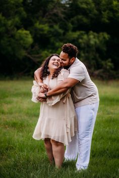 a man and woman hugging in the grass with trees in the background