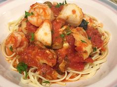 a white plate topped with pasta covered in sauce and shrimp on top of tomato sauce