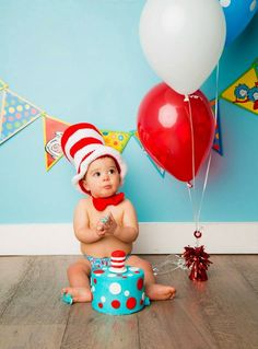 a baby sitting on the floor wearing a cat in the hat outfit and eating cake