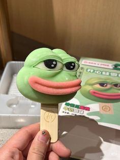 a hand holding a green popsicle with googly eyes and tongue sticking out from it