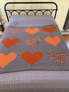 a crocheted bedspread with orange and gray hearts on the bed spread