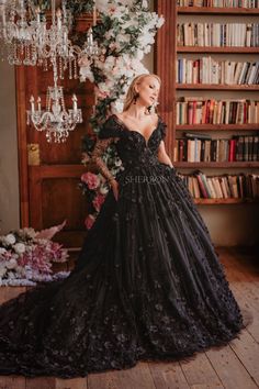 a woman standing in front of a bookshelf wearing a black dress with flowers on it