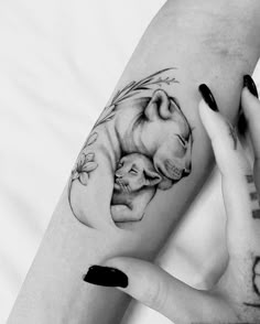 two hands holding each other with tattoos on their arms and the arm is covered in an image of a mother bear hugging her baby