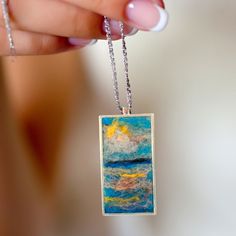 a woman holding up a necklace with an ocean scene painted on the front and back