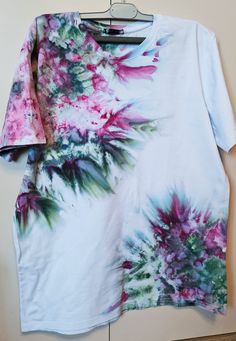 a white t - shirt with pink and green flowers on it hanging from a hanger