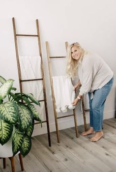 a woman standing next to a ladder with towels on it and a potted plant