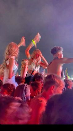 a group of people standing around each other at a music festival with their arms in the air