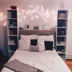 a white bed topped with lots of pillows next to a book shelf filled with books