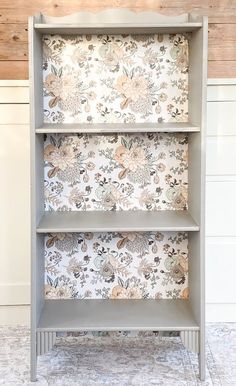 a grey bookcase with floral wallpaper on the front and back sides, against a white background