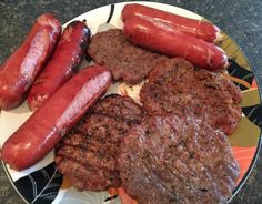 a plate with sausages, hot dogs and hamburger patties sitting on top of it