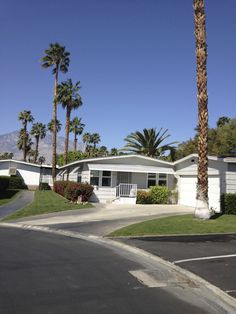 a white house with palm trees in the front yard and on the other side is a street