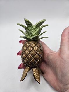 a small gold pineapple shaped object in someone's hand