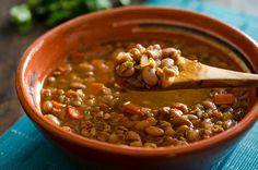 a wooden spoon in a bowl filled with lentulas and beans on a blue place mat