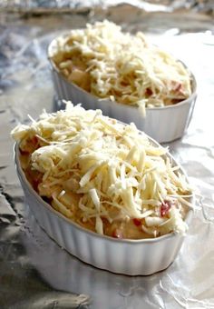 two white dishes filled with food sitting on top of aluminum foil covered in grated cheese