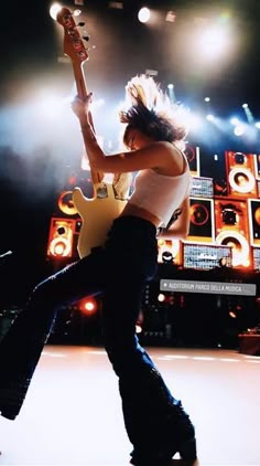 a woman in white shirt and black pants playing guitar on stage with lights behind her