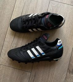 two black adidas shoes sitting on top of a wooden floor next to each other