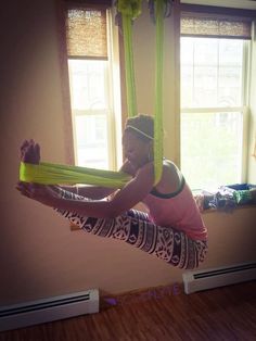 a woman doing aerial acrobatics in front of a window on a yoga mat