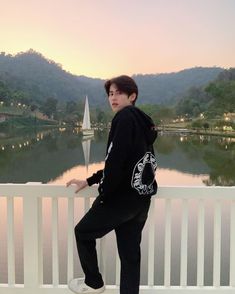 a young man standing on top of a white fence next to a lake