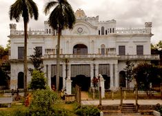 an old white building with palm trees in front