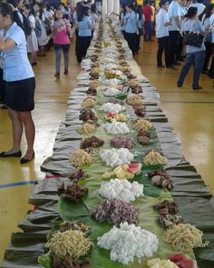 a long table with many different types of food on it and people in the background