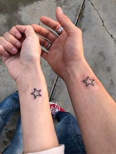 two people holding hands with small tattoos on their wrist and one has a star in the middle