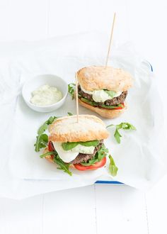 two sandwiches with lettuce, tomato and mayonnaise sit on parchment paper