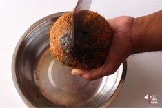 a person holding a coconut in their hand over a metal bowl with a knife sticking out of it