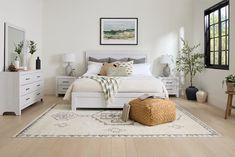 a bedroom with white furniture and wood flooring is pictured in this image, there is a large mirror on the wall above the bed