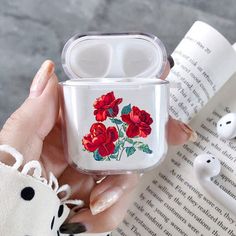 a woman holding an airpods case with red roses on it