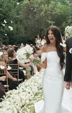 a bride and groom walking down the aisle with white flowers in their hand as they exit