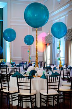 blue balloons are hanging from the ceiling above tables in a room with white linens and black chairs