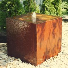 a square metal object sitting on top of a rock covered ground next to trees and bushes