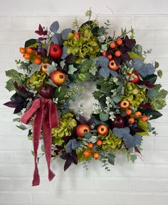 a wreath with apples, leaves and berries hanging on a wall next to a brick wall