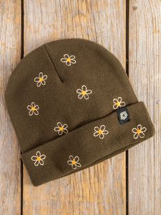 a brown beanie with yellow and white flowers on it sitting on a wooden surface