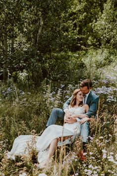 a man and woman sitting in the middle of a field with wildflowers around them