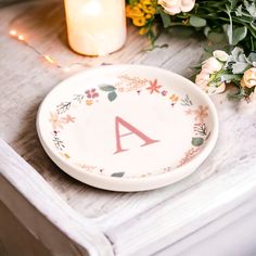 a plate with the letter a painted on it sitting next to flowers and a candle