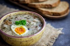 a bowl of soup with an egg on top and bread slices in the back ground